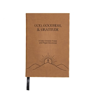 May include: A brown leather-bound journal with the title "GOD, GOODNESS, & GRATITUDE" and the subtitle "A Daily Christian Praise and Prayer Devotional". The cover features a simple line drawing of a mountain with a cross on top and a sun rising behind it.