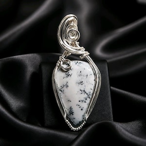 May include: A teardrop-shaped pendant featuring a white stone with black dendritic inclusions, encased in a polished silver wire-wrapped setting. The wirework forms intricate loops and coils at the top, creating a secure frame for the stone.