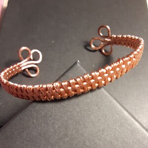 May include: A copper wire bracelet with a woven design and two decorative loops on each end.