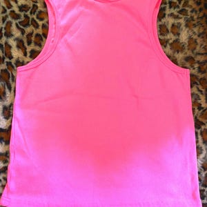 May include: A bright neon pink sleeveless tank top featuring a ribbed texture throughout the fabric. The garment has a classic scoop neckline and wide shoulder straps, with a straight hemline at the bottom, providing a simple and clean design.