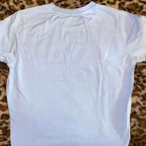 May include: A plain, light blue short-sleeved t-shirt with a crew neckline. The garment features a simple, solid-colored design with visible stitching along the sleeves and the bottom hem, presented in a clean and straightforward construction.