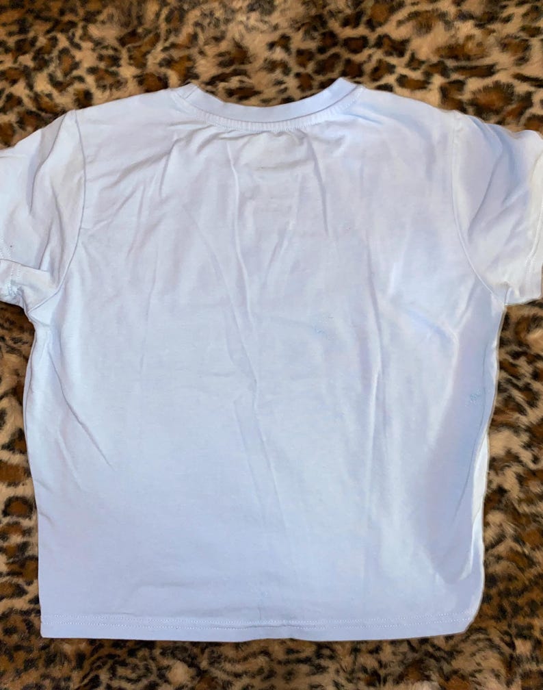 May include: A plain, light blue short-sleeved t-shirt with a crew neckline. The garment features a simple, solid-colored design with visible stitching along the sleeves and the bottom hem, presented in a clean and straightforward construction.