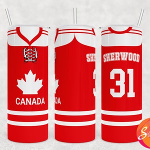 Pode incluir: Um copo vermelho e branco com um design de camisa de hóquei. O copo tem uma folha de bordo branca e a palavra "CANADA" na frente. A parte de trás do copo tem o nome "SHERWOOD" e o número "31". Inclui uma palhinha prateada.
