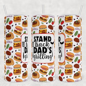 May include: White tumbler with a black and white design of hamburgers, pickles, onions, and tomatoes. The text "Stand back Dad's grilling" is printed in black on a red rectangle.
