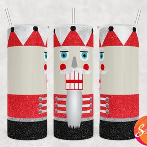Op de afbeelding: Een roestvrijstalen tumbler met een zwarte deksel en een rietje, versierd met een rood en wit notenkrakerontwerp. De tumbler is versierd met glitter.