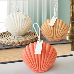 May include: Three seashell-shaped candles in white, orange, and coral colours. Each candle has a white tag attached to a string.