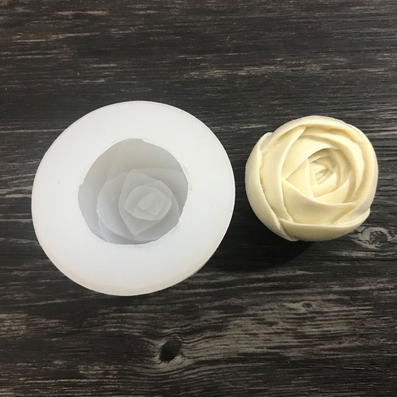 May include: A white silicone mold shaped like a rose, next to a white rose-shaped soap.