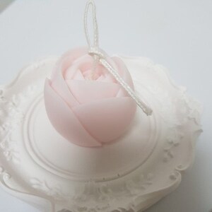 May include: A delicate pink rose-shaped candle with a white wick and a white string attached to the top.
