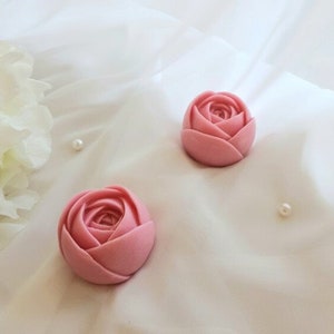 May include: Two pink rose-shaped soaps on a white background. The soaps are made to look like real roses.