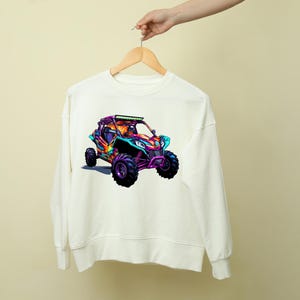 May include: White sweatshirt with a colorful graphic of an off-road vehicle. The vehicle is a bright pink, blue, and green color with black wheels.