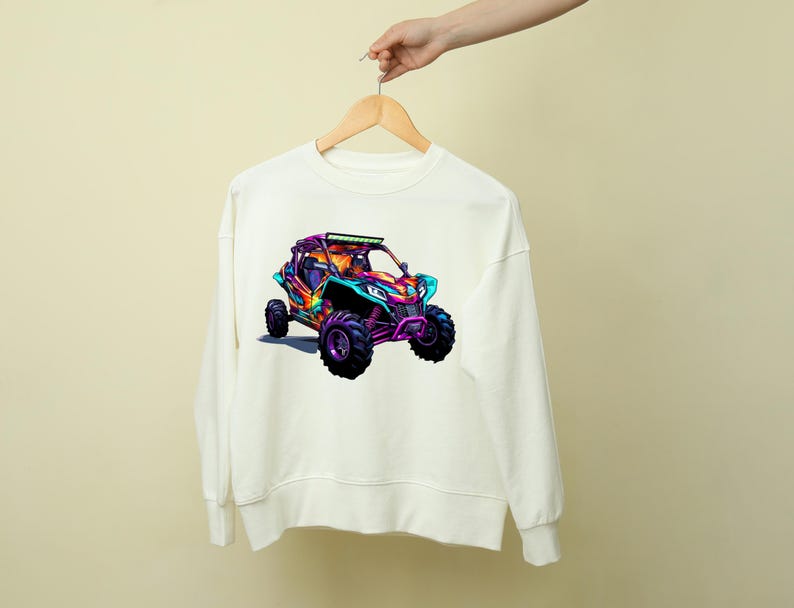 May include: White sweatshirt with a colorful graphic of an off-road vehicle. The vehicle is a bright pink, blue, and green color with black wheels.