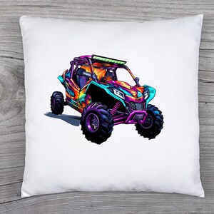 May include: A white pillow with a colorful illustration of a side-by-side off-road vehicle. The vehicle is painted in shades of pink, purple, blue, and green. It has a roll cage and a light bar on the roof.