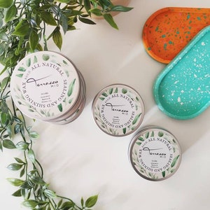 Peut inclure: Trois boîtes en argent de cire 100% naturelle pour sceller et faire briller. Les boîtes ont un motif floral vert et blanc avec le texte "Terrazzo Mio" et "100% Cire Naturelle Scellant et Brillant" sur le devant. Les boîtes sont posées sur une surface blanche avec une plante verte et deux plateaux mouchetés.