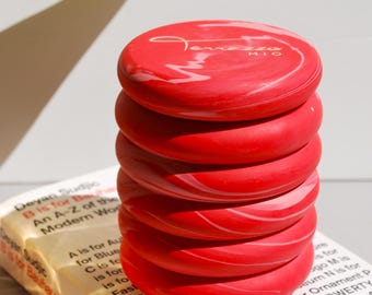 Pode incluir: Uma pilha de seis  copos de cerâmica marmoreados em vermelho e branco com a palavra "MIO" em letras douradas no copo superior. Os copos estão empilhados em cima de um livro.