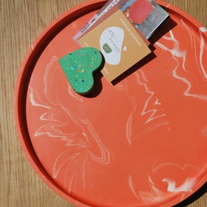 Puede incluir: Una bandeja de color coral con vetas blancas, con un adorno en forma de corazón verde y una tarjeta de visita que dice "Handmade Homeware" y "Jewels & Co."