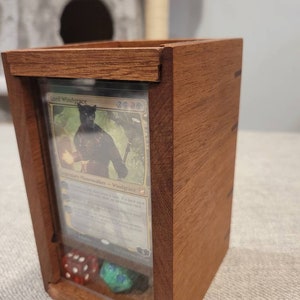 May include: A wooden card holder with a clear front panel, displaying a card with the text "Lord Windgrace". Inside are dice. The holder is made of reddish-brown wood.