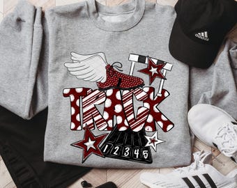 May include: A gray sweatshirt with a track and field design. The design includes the word "TRACK" in red and white polka dot letters, a winged running shoe, hurdles, and stars. A black Adidas cap and white sneakers are also visible.