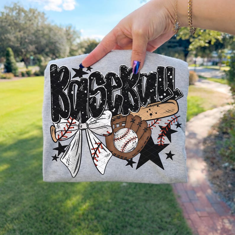 K&ouml;nnte beinhalten: Ein graues T-Shirt mit einem Baseball-Motiv. Das Design zeigt das Wort "Baseball" in einer fetten Schrift, einen Baseballschl&auml;ger, einen Handschuh, einen Baseball, eine Schleife und Sterne. Die Grafik ist in Schwarz, Wei&szlig; und Braun gehalten.