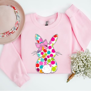 May include: Pink sweatshirt featuring a colourful polka dot bunny design. The bunny has a pink bow and a white fluffy tail.