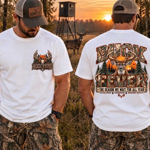 May include: A white t-shirt featuring a small graphic on the front left chest and a large graphic on the back. Both graphics depict a deer head, pine trees, and a sunset with the text BUCK FEVER. The back includes THE SEASON WE WAIT FOR ALL YEAR.