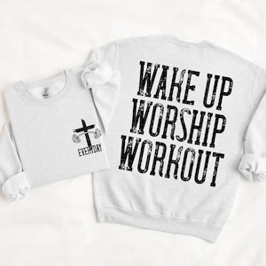 May include: Two light gray sweatshirts. One has a cross and barbell graphic with the word "EVERYDAY". The other has the words "WAKE UP WORSHIP WORKOUT" in large black letters.