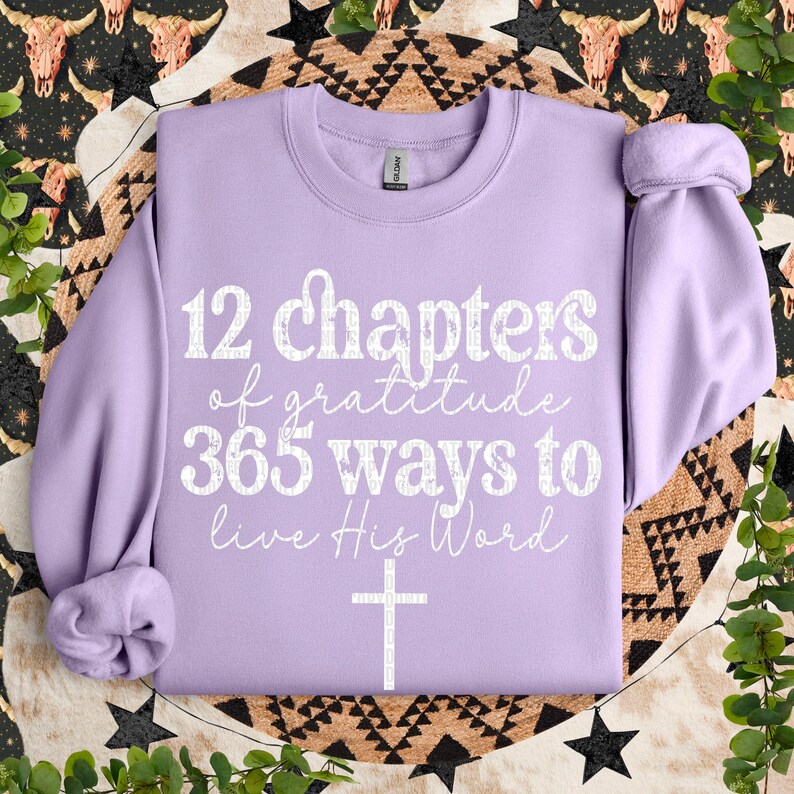 May include: A lavender sweatshirt with the text "12 chapters of gratitude 365 ways to live His Word" and a white cross.
