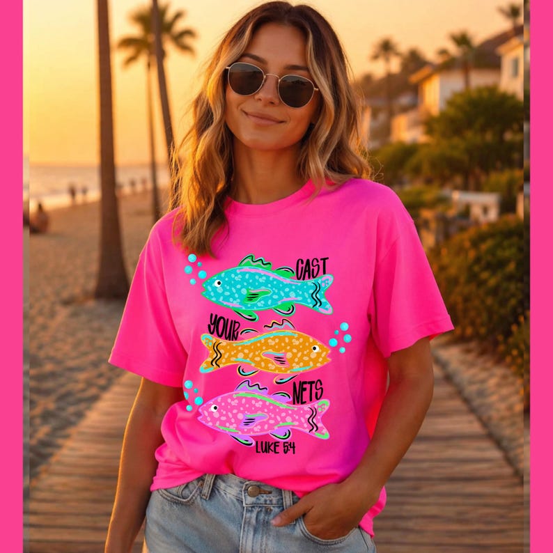 May include: A bright pink t-shirt featuring three colorful fish illustrations with the words "CAST YOUR NETS" and "LUKE 5:4". The fish are teal, yellow, and pink, with green and blue accents. The shirt is worn by a person with sunglasses.