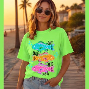 May include: A neon green t-shirt featuring three colorful fish illustrations. The text "CAST YOUR NETS" and "LUKE 5:4" are printed on the shirt. The fish are blue, orange, and pink.