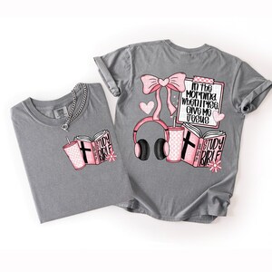 May include: Two gray t-shirts with pink and black graphics. One shirt features a book, a drink, and the words "Study Bible." The other shirt has a bow, headphones, a drink, a notepad with text, and a book. The text on the notepad says "In the morning when I rise, give me Jesus."