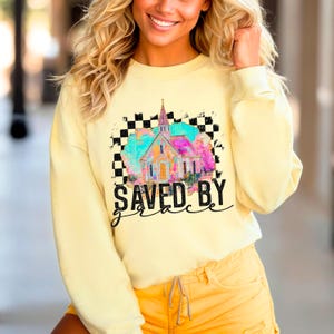 May include: Yellow sweatshirt with a colorful church graphic and the text "SAVED BY grace" in black.