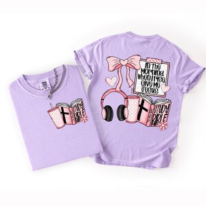 May include: Two light purple t-shirts with graphic designs. One shirt features a pink Study Bible, a drink, and a cross. The other shirt has a bow, headphones, a drink, and the text "In the morning when I rise, give me Jesus."