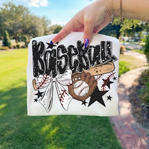 K&ouml;nnte beinhalten: Wei&szlig;es T-Shirt mit Baseball-Design. Das Design zeigt das Wort "Baseball" in schwarzer Graffiti-Schrift, einen Baseballschl&auml;ger, einen Baseballhandschuh, einen Baseball, eine Schleife und schwarze Sterne.