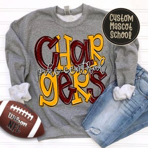 Pode incluir: Uma camisola cinzenta de gola redonda com o texto CHARGERS em letras grandes amarelas e bordeaux aos quadrados e o texto pike central em escrita branca. Uma bola de futebol americano Wilson e calças de ganga azuis estão junto à camisola.
