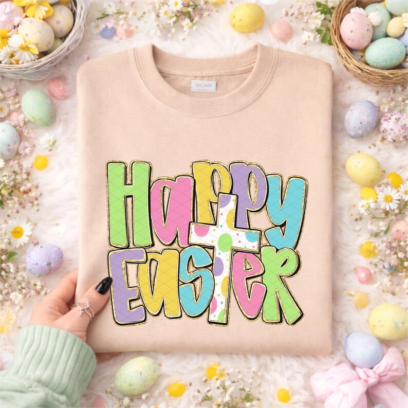 May include: A beige sweatshirt with the words "Happy Easter" in colorful bubble letters and a cross. The letters are outlined in gold and filled with pastel colors. The sweatshirt is surrounded by Easter eggs and flowers.
