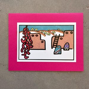 May include: A rectangular greeting card with a bright pink border framing a central illustration. The drawing depicts two tan adobe structures, a hanging cluster of red chili peppers, a wooden ladder, and small colorful decorative shapes.