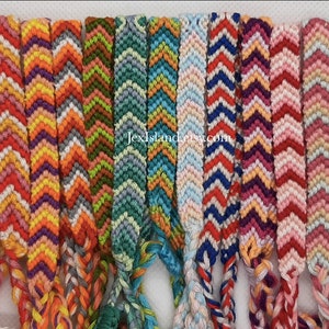 Peut inclure: Un ensemble de 14 bracelets d'amitié colorés avec des motifs en chevron. Les bracelets sont faits de fil à broder et présentent une variété de combinaisons de couleurs, notamment le rouge, l'orange, le jaune, le vert, le bleu, le violet, le rose et le noir.
