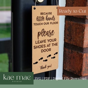 May include: A brown sign with the text "Because little hands touch our floor please leave your shoes at the door" and a row of footprints. The sign is hanging on a door with a brick wall in the background. The text "Ready to Cut" is in the top right corner of the image.