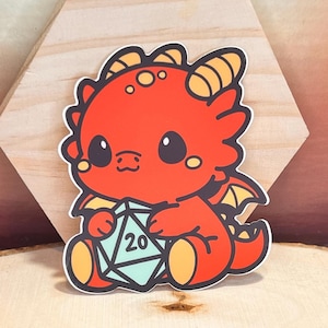 May include: A red cartoon dragon with yellow horns and wings is holding a blue twenty-sided die. The dragon has a cute, cartoonish expression.