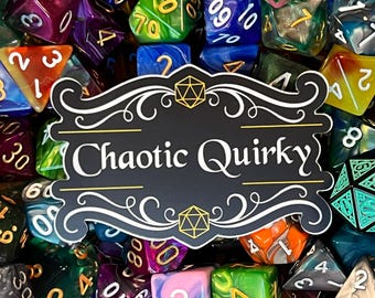 May include: A black and white sticker with gold accents featuring the text "Chaotic Quirky" in a decorative font. The sticker is surrounded by a variety of colorful dice with different numbers and symbols.