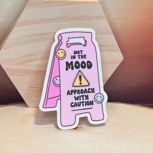 Könnte beinhalten: Rosa-weißer Warnschild-Aufkleber mit dem Text "Nicht in Stimmung. Mit Vorsicht nähern." und einem gelben Ausrufezeichen.