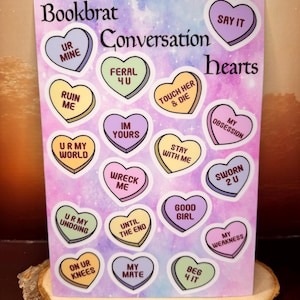 May include: A set of 16 conversation heart stickers with various sayings on them. The stickers are on a pink and blue background with a galaxy design. The sayings include "Say It", "Ur Mine", "Feral 4 U", "Touch Her & Die", "My Obsession", "Ur My World", "Im Yours", "Stay With Me", "Wreck Me", "Until The End", "Good Girl", "Sworn 2 U", "My Weakness", "On Ur Knees", "My Mate", and "Beg 4 It".