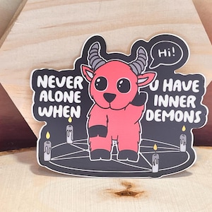 May include: A red cartoon devil with horns and a pentagram is standing on a black background with the text "Never alone when you have inner demons" and "Hi!" in a speech bubble.