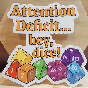May include: A white sticker with the text "Attention Deficit... hey, dice!" in orange. The sticker features a group of colorful dice with different numbers.