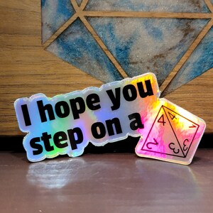 May include: A holographic sticker with the text "I hope you step on a" and a holographic sticker of a 4-sided die with the numbers 2, 3, 4, and 1.