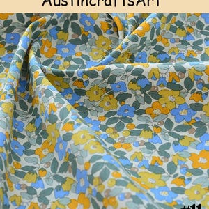 K&ouml;nnte beinhalten: Stoff mit einem dichten Blumenmuster aus gelben und blauen Bl&uuml;ten, gr&uuml;nen Bl&auml;ttern und kleinen runden orangefarbenen Beeren auf wei&szlig;em Grund. Der Text Austin crafts Art und die Nummer 11 sind auf dem Bild zu sehen.
