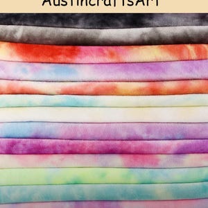 May include: A stack of folded fabric pieces featuring various tie-dye patterns in colors including black, gray, orange, purple, blue, yellow, pink, and green. The text AustincraftsArt is printed at the top of the image. The fabric has a soft, plush texture.