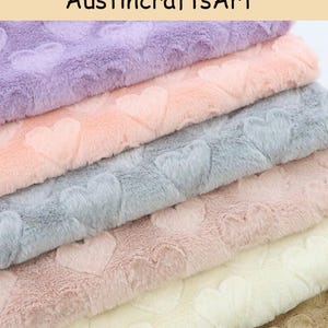 May include: A stack of five folded pieces of plush fabric featuring an embossed heart pattern. The colors from top to bottom are lavender, light peach, light gray, dusty rose, and cream. The text Austin crafts Art is visible at the top.