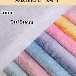 May include: A collection of plush faux fur fabric squares in various pastel colours including white, pink, blue, purple, and yellow. The text Austin crafts Art, 5mm, and 50*50cm is visible on the white fabric. The fabric has a soft texture.