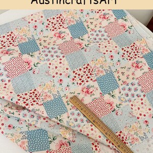 May include: A fabric featuring a patchwork pattern of squares with floral prints in pink, red, and yellow, alongside blue and white polka dots. A wooden ruler is placed diagonally across the fabric, showing measurements up to 26 centimeters.