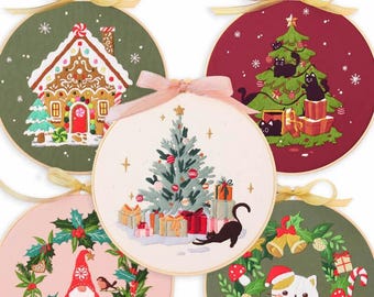 May include: Five round embroidery hoops with different Christmas themes. The hoops are decorated with embroidery of a gingerbread house, a Christmas tree with cats, a Christmas tree with presents, a wreath with a gnome, and a wreath with a cat.